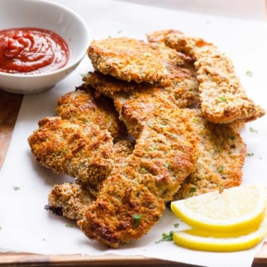 baked healthy almond crusted chicken tenders being served on a plate with lemon wedges and ketchup