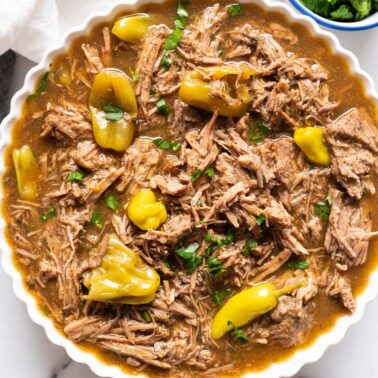 Instant Pot Mississippi pot roast with peperoncini peppers and parsley in a bowl.