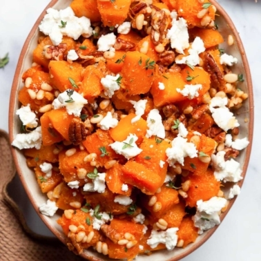 Sauteed butternut squash with pine nuts and goat cheese in a bowl.