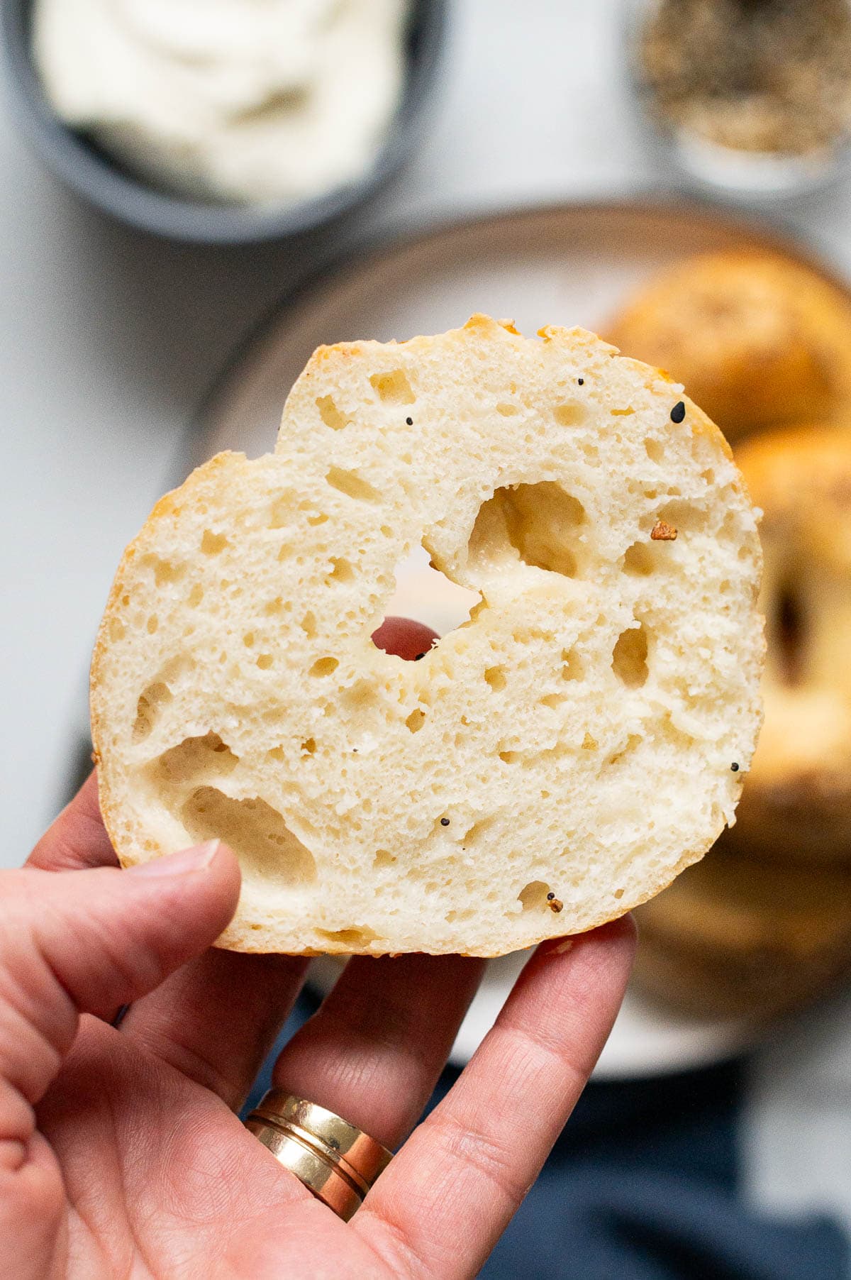Person holding sliced Greek yogurt bagel showing texture inside.