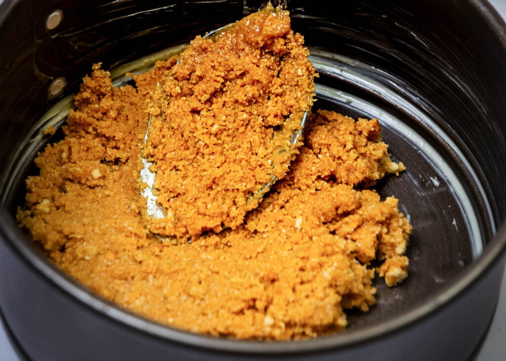Adding graham cracker crust to a springform pan.