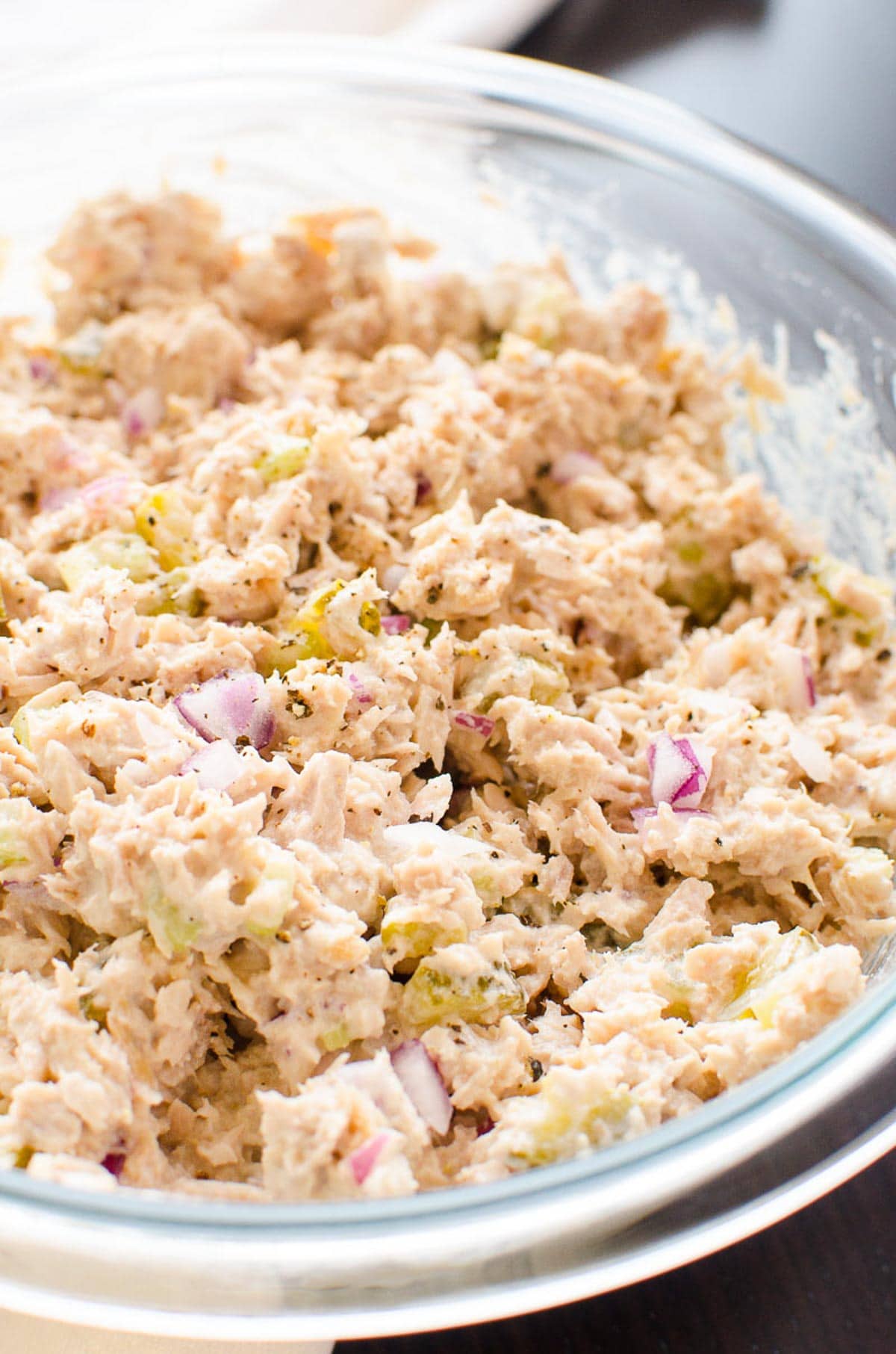 Healthy tuna salad in a glass bowl garnished with ground black pepper and red onion.
