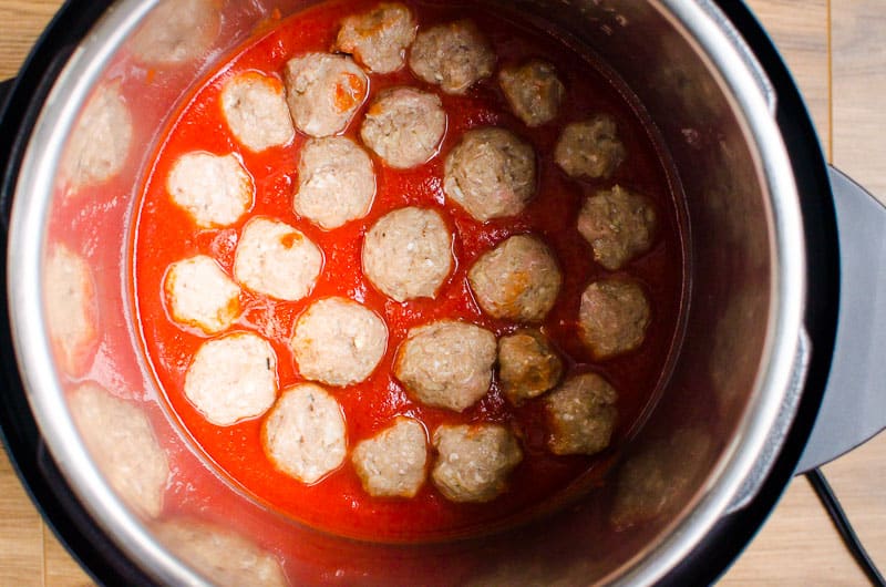 Uncooked meatballs placed in sauce in the Instant Pot.